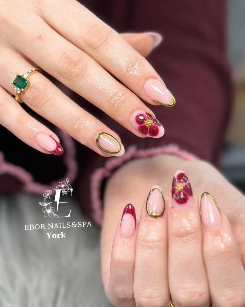 Nude almond nails with burgundy tips, gold outlines and a painted flower